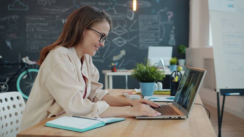 Woman working on a laptop in front of a blackboard
